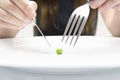 Woman eating a small green pea using knife and fork. Extreme dieting concept. Close-up, selective focus Royalty Free Stock Photo