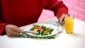 Woman eating vegetable salad with fork and knife, fresh orange juice on table Royalty Free Stock Photo