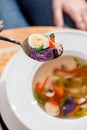 Woman eats broth with quail eggs, herbs, carrots and other vegetables in a white plate on a yellow set on the table. Royalty Free Stock Photo