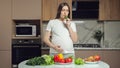 Woman eats vegetables stroking pregnant belly in kitchen
