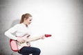 Woman with an electric guitar near a concrete wall