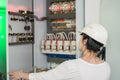 A woman electrician opens an electrical box.A girl in a white helmet checks the fuse box. View from the back. Selective focus