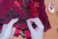 Woman embroider red vest with beads on wooden table