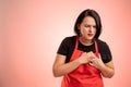 Woman employed at supermarket with red apron and black t-shirt suffering heart ache or breast pain, cardiac problems Royalty Free Stock Photo