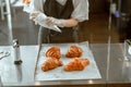 Employee holds confectioner sleeve with delicious cream to decorate croissants in bakery shop