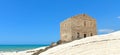 Woman on empty white beach with old ruins of abandoned stone house on the rocks and summer blue sky and sea in background in Sicil Royalty Free Stock Photo