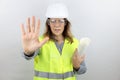 Woman engineer with hardhat holding plans under arm and with open hand doing stop sign with serious and confident expression