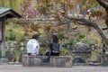 Woman enjoyed sitting in the garden with red and orange tree leaves in autumn background in Kyoto