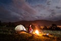 Woman enjoying a bonfire near tent under cloudy sky