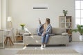 Woman enjoying cool fresh air in her living room with air conditioner on the wall