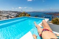 Woman relaxing by infinity pool in Greece, Santorini. Sea view with Fira town overlooking. Travel lifestyle background Royalty Free Stock Photo