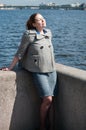 Woman enjoying the sunlight while standing on granite embankment, female dressed coat and skirt