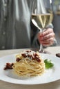 Woman enjoying tasty spaghetti with sun-dried tomatoes and cheese and wine at wooden table in restaurant, closeup. Royalty Free Stock Photo