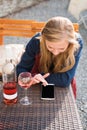 Woman enjoying wine in city street restaurant terrace. Wine tasting tourist girl sitting at the table in sidewalk cafe and using Royalty Free Stock Photo