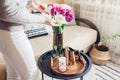 Woman enjoys tulips flowers put in vase on table with tray, watering can and candle. Interior and spring decor at home Royalty Free Stock Photo