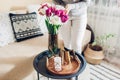 Woman enjoys tulips flowers put in vase on table with tray, watering can and candle. Interior and spring decor at home Royalty Free Stock Photo