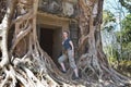 woman at an entrance to the destroyed covered with roots of trees temple Prasat Chrap in the Koh Ker temple complex, Siem Reap, C