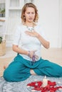 Woman in ethnic costume practicing yoga in front of candles and red rose petals, hands with mehendi and mala beads on the heart Royalty Free Stock Photo