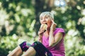 Woman exercising in park while listening to music. Mature woman eat banana resting after exercise Royalty Free Stock Photo