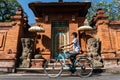 A woman exercising riding a bicycle during summer in Bali. Traditional Balinese doors made of red bricks make for a beautiful and