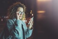 Woman in eye glasses holding hands smartphone in night atmospheric city.Female hands using mobile phone.Closeup on