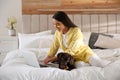 Young woman with eye patches working on laptop near her dog in bedroom. Home office concept Royalty Free Stock Photo