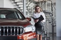 Woman in eyewear, black skirt and white shirt stands near the red automobile