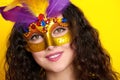 Woman face closeup in carnival masquerade mask with feather, beautiful girl portrait on yellow color background, long curly hair Royalty Free Stock Photo