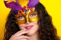 Woman face closeup in carnival masquerade mask with feather, beautiful girl portrait on yellow color background, long curly hair Royalty Free Stock Photo