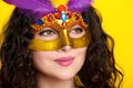 Woman face closeup in carnival masquerade mask with feather, beautiful girl portrait on yellow color background, long curly hair Royalty Free Stock Photo
