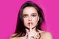 Woman face, finger on her lips. Silence gesture. Portrait of sensual young female model.