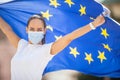 Woman in a face mask holding an European union flag behind her back with arms up Royalty Free Stock Photo