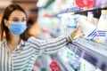 Woman in face mask shopping in supermarket, taking milk Royalty Free Stock Photo