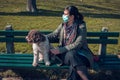 woman with face mask sitting on park bench with her dog Royalty Free Stock Photo