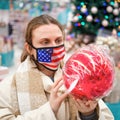 Woman in face mask with usa flag buys christmas baubles in gift shop. Lifestyle, a celebration of the coronavirus pandemic Royalty Free Stock Photo