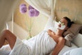 Woman and facial clay mask on face and cucumber on eyes relaxing in bed at home Royalty Free Stock Photo