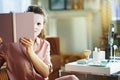 Woman with facial mask looking out from book showing half face