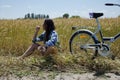 Woman farmer sitting on a wheat field. Young pretty farmer woman on farmland with bicycle. Beautiful girl in plaid shirt in golden Royalty Free Stock Photo