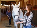 Woman farmer standing with horse, male worker cleaning floor