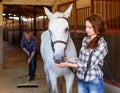 Woman farmer standing with horse, male worker cleaning floor