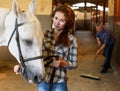 Woman farmer standing with white horse, man cleaning floor Royalty Free Stock Photo