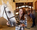 Woman farmer standing with white horse, man cleaning floor Royalty Free Stock Photo