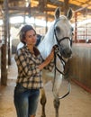 Woman farmer standing with white horse at stabling indoor Royalty Free Stock Photo
