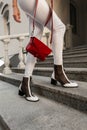 Woman in fashion white denim clothes in elegant shoes with a red bag stands on the stone steps in the city