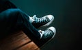 A woman in fashionable blue jeans and sneakers is sitting on a wooden pier, his legs dangling over the surface of the lake water. Royalty Free Stock Photo