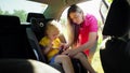 A woman fastens the seat belt of her child who is sitting in a car seat.