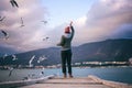 Woman feeding seagulls standing on city pier at sunset, beautiful landscape Royalty Free Stock Photo