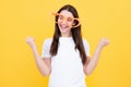 Woman feeling cool and awesome. Excited happy funny young woman in party glasses in the shape of a heart on a yellow