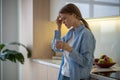 Woman feeling terrible pain in head drinking water on kitchen at home with closed eyes.