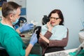 Woman feeling toothache, touching cheek with hand at dental clinic. Senior dentist trying to help with dental tool Royalty Free Stock Photo